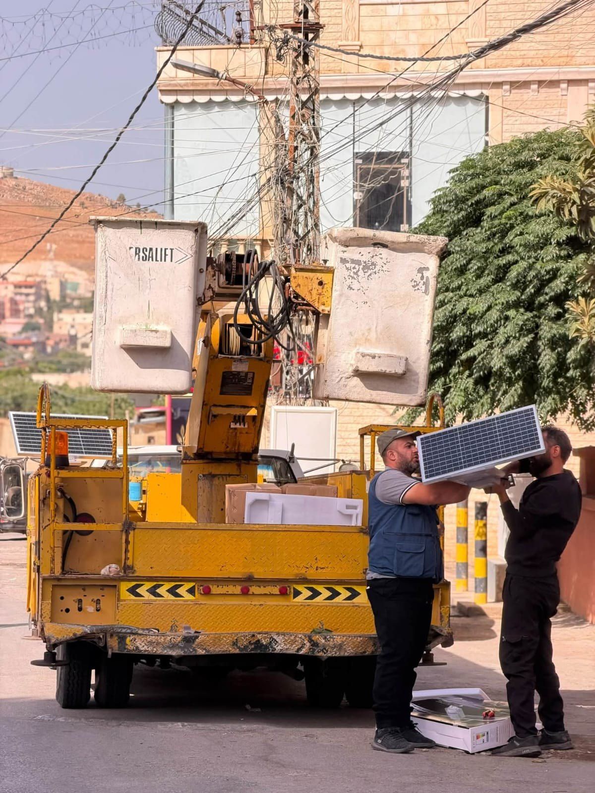 عاملان يركّبان لوح إنارة بالطاقة الشمسية على عمود في أحد شوارع البلدة